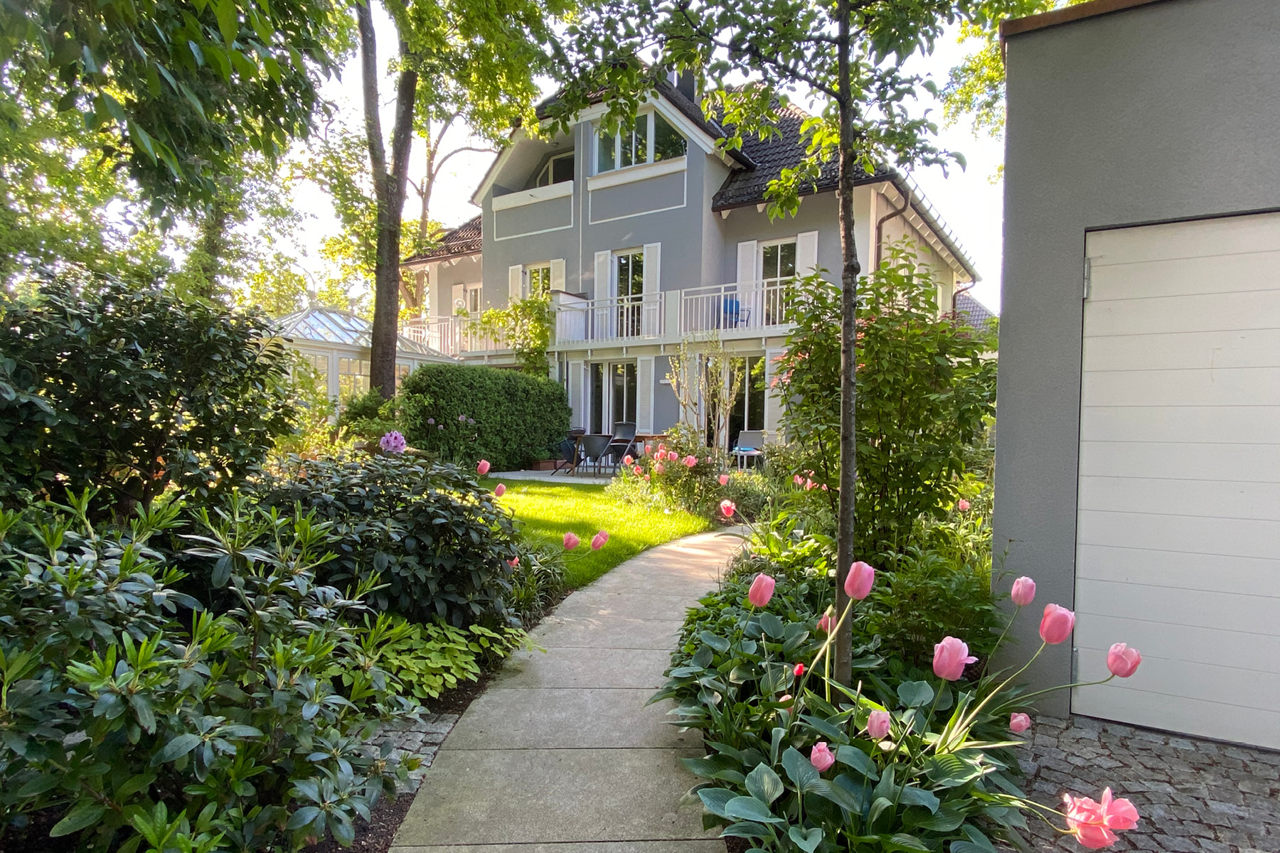 Blick in den Garten, im Hintergrund eine Villa, ein geschwungener Granitweg führt zu dem Haus.