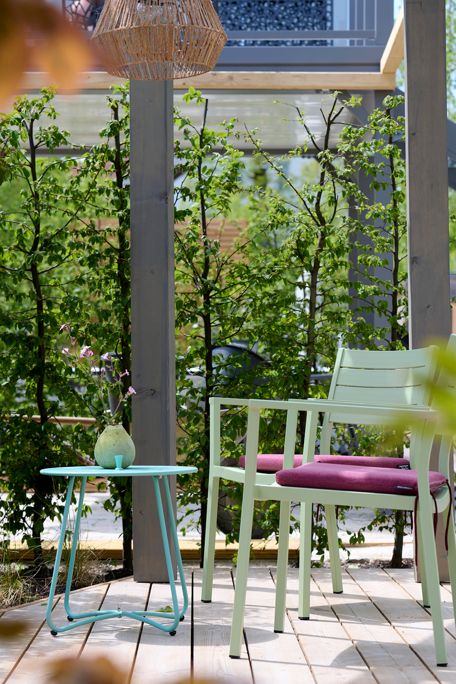 Blick unter der Holzpergola auf die mintgrünem Aluminiumstühle. Sie stehen auf dem Thermoholzdeck.