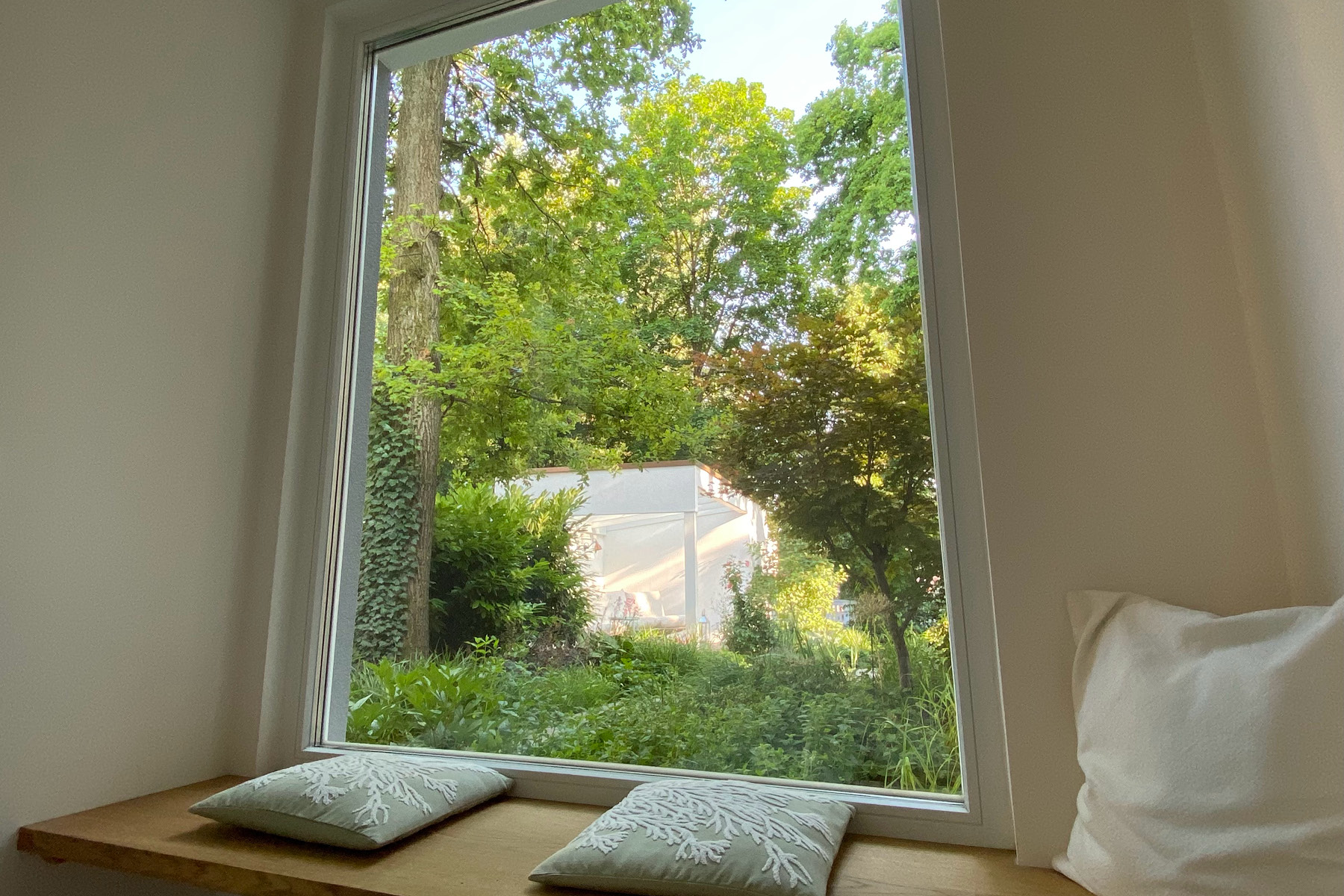 Eine Teilansicht der neugestalteten Garderobe, die eine Sitzbank im Kissen am Fenster erhalten hat. Der Blick führt in den Garten auf die Gartenlounge.